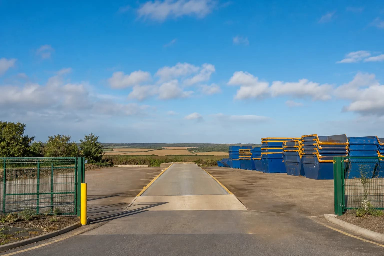 The UK Skip Hire depot with neatly stacked steel skips under a bright sky
