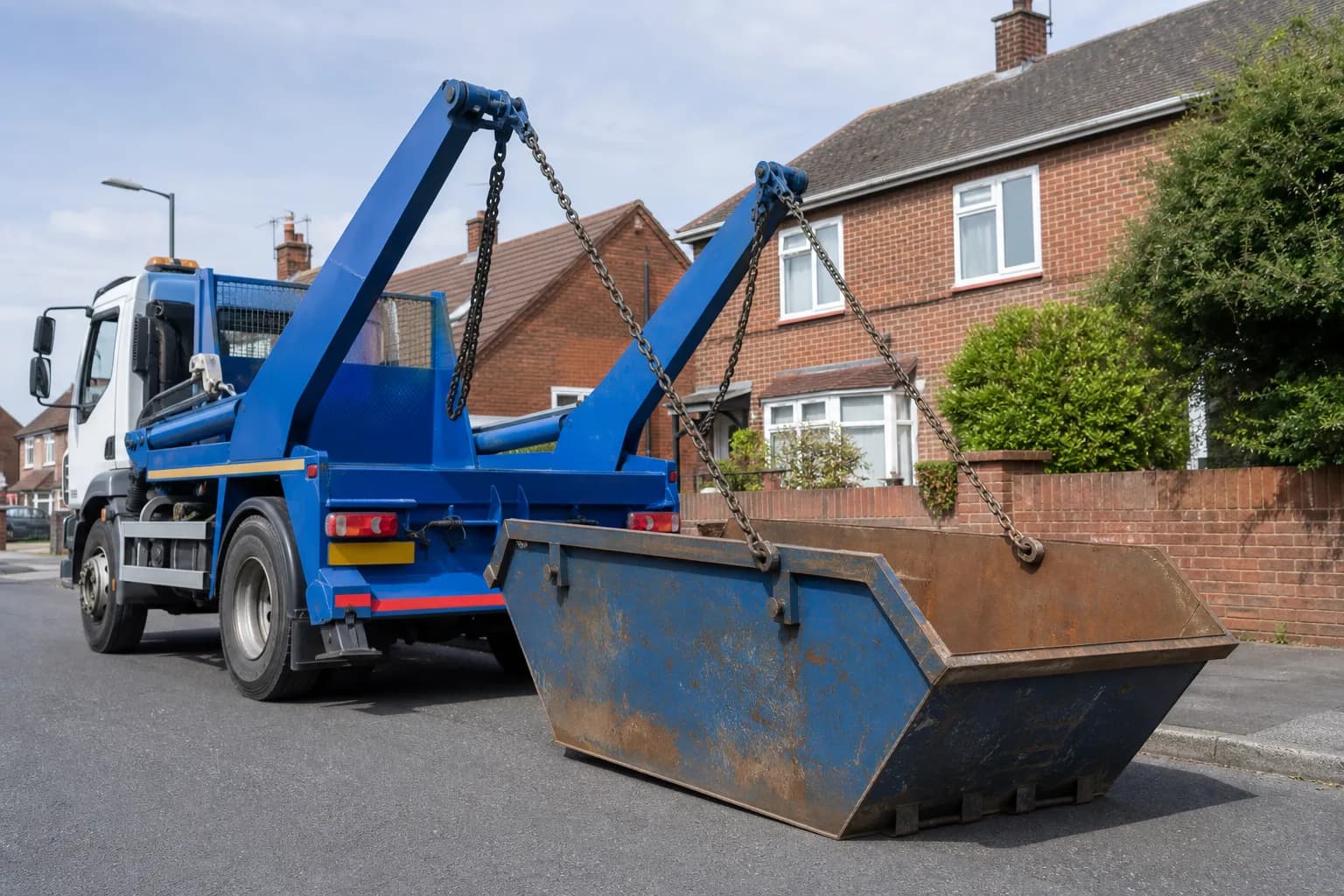 A skip lorry lowering an empty steel skip onto a residential street