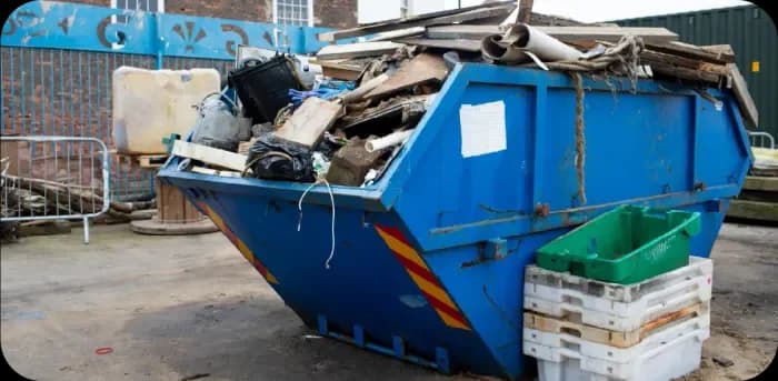 A blue UK Skip Hire skip filled with mixed waste outside a property